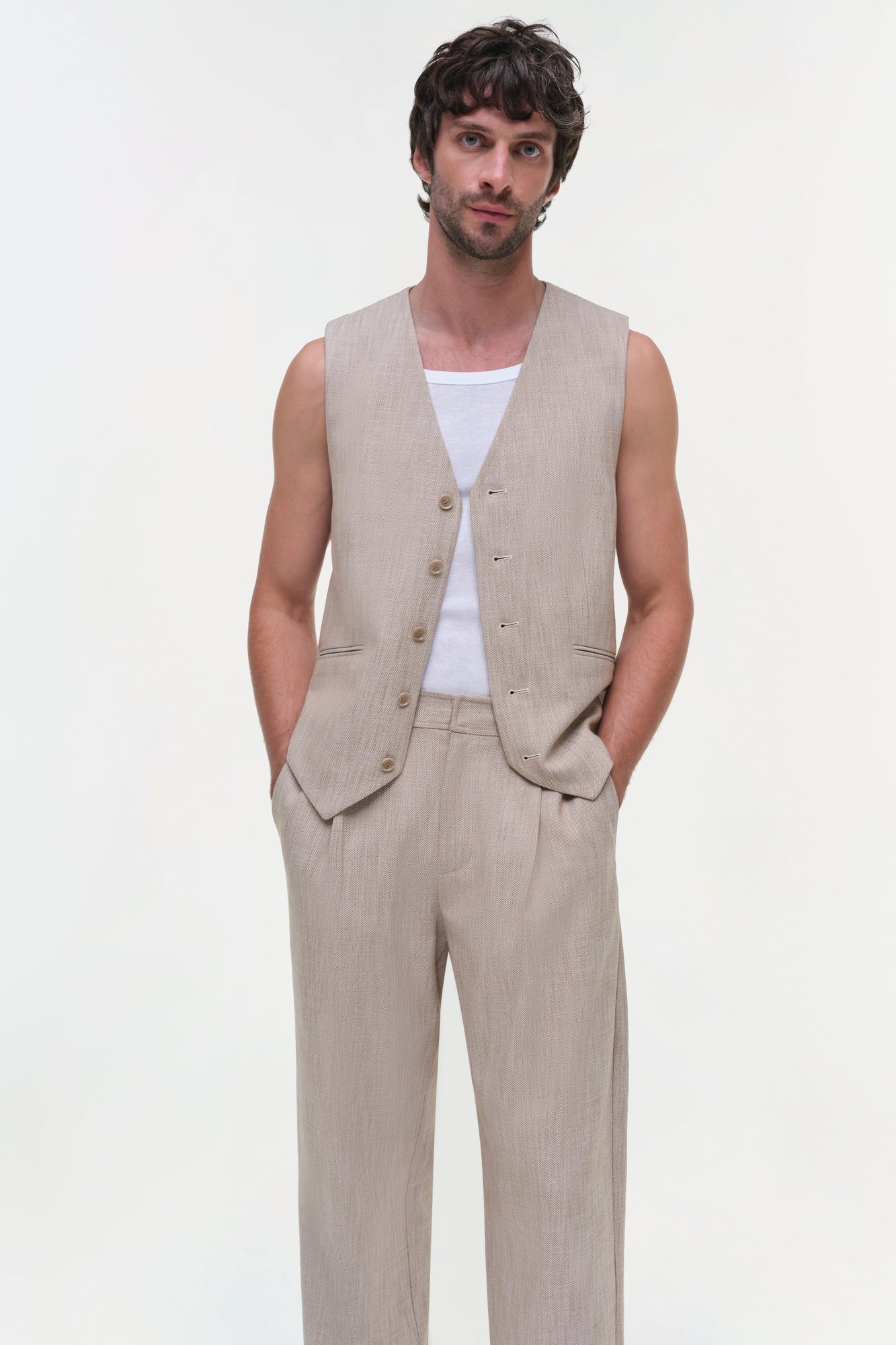 Man wearing a beige linen vest with button front over a white t-shirt, paired with matching beige trousers.