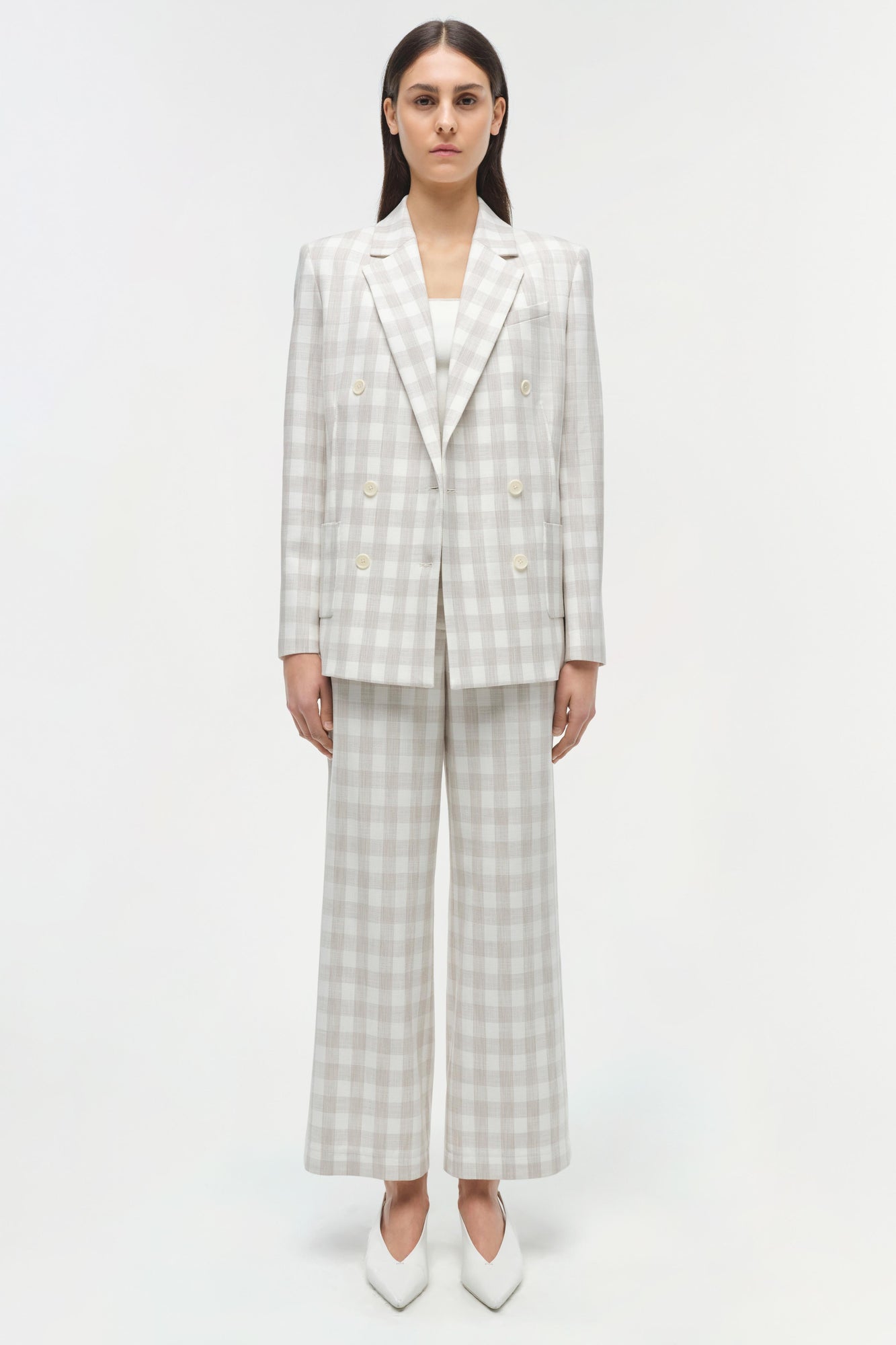 Woman wearing a light gray and white checkered double-breasted blazer with matching wide-leg trousers and white pointed-toe b