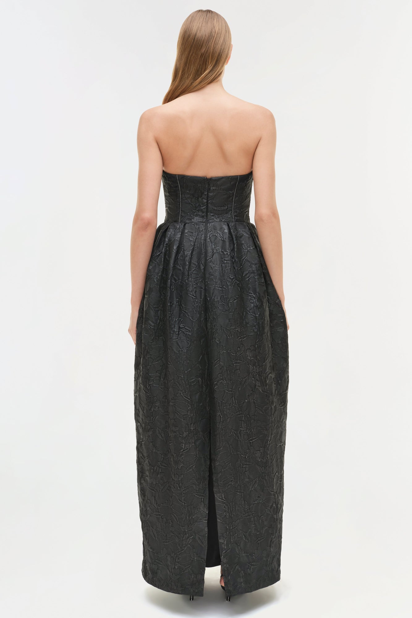 Black jacquard bustier gown with strapless neckline and floor-length skirt with side slit, back view.