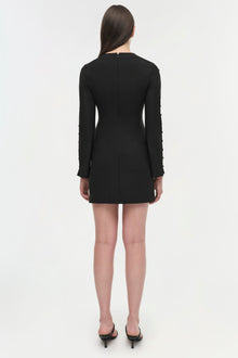 Woman wearing a black long-sleeve mini dress with a center back seam, shown from behind.