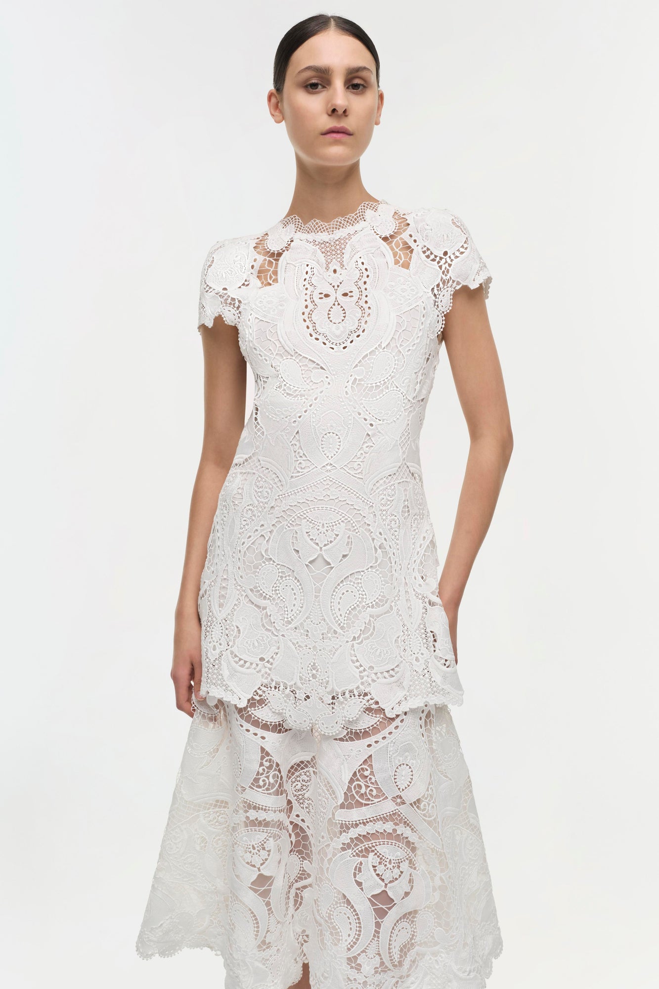 White lace dress with short sleeves, ornate cutout patterns, and tiered ruffle hem.