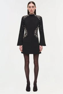 Black mini dress with silver crystal embellishments on shoulders, sides, and sleeves; long flared sleeves and high neckline.