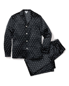 The Mens Silk Pajama Set in Black Art Nouveau by Petite Plume showcases black luxurious pajamas with white polka dots. Made from soft mulberry silk, the set includes a long-sleeve button-up top and pants, elegantly displayed flat against a white background.