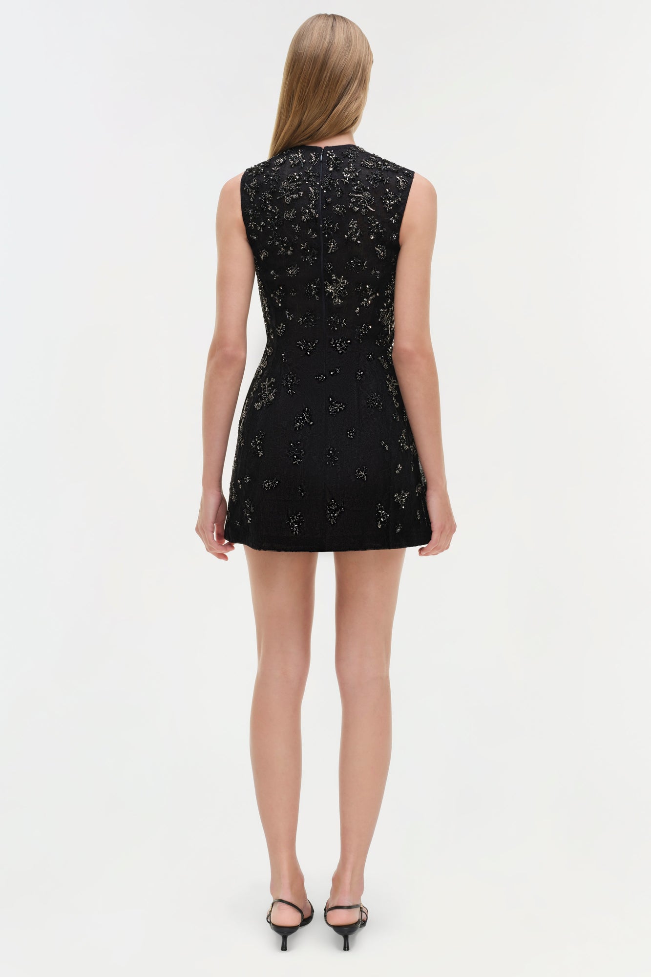 Black lace sleeveless mini dress with embellished detailing, shown from back on model wearing black heels.
