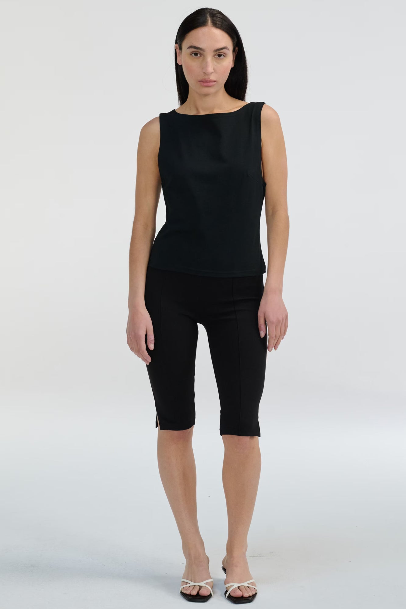 Woman wearing a black sleeveless top and black capri pants on a white background