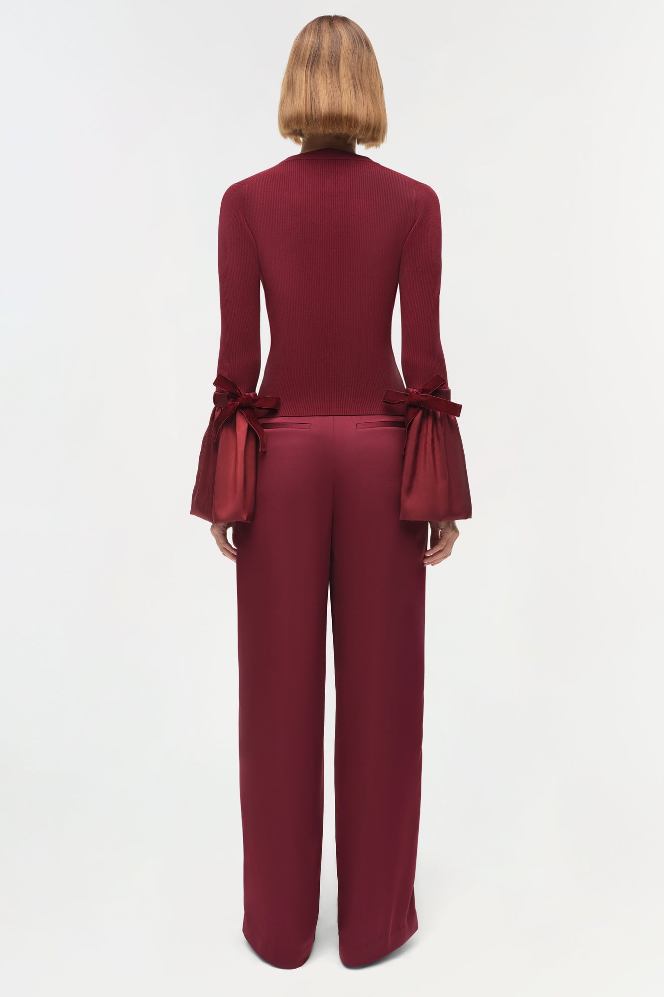 Burgundy knit top with flared sleeves featuring bow ties at the cuffs, shown on model from back view.