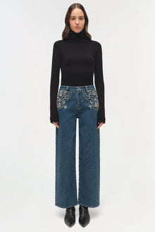 Blue denim crop jeans with pearl embellishments on pockets, paired with black turtleneck and boots.
