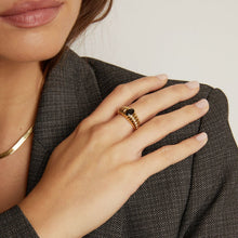 Close-up of a hand wearing a gold ring with a black stone, holding a textured gray fabric.