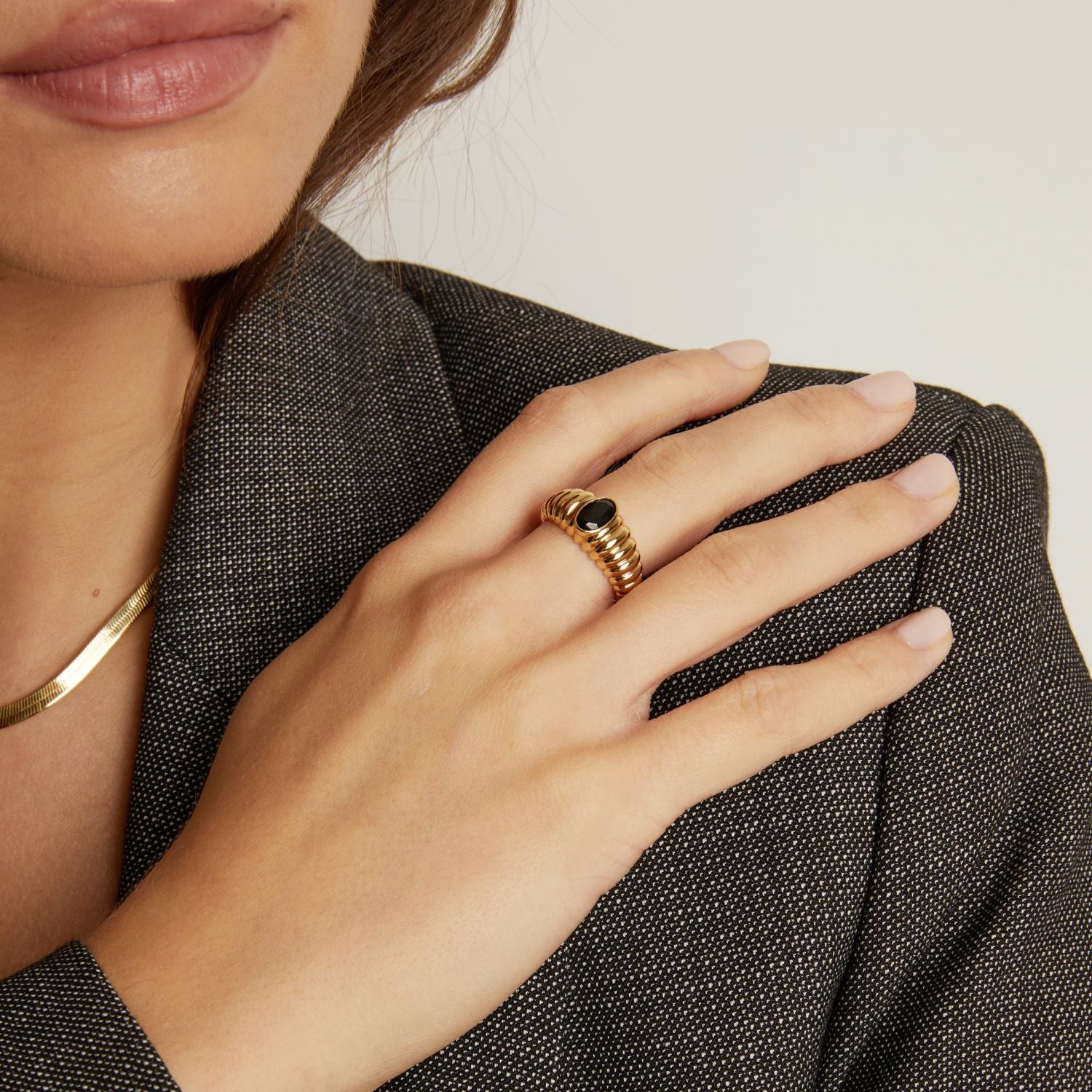 Close-up of a hand wearing a gold ring with a black stone, holding a textured gray fabric.