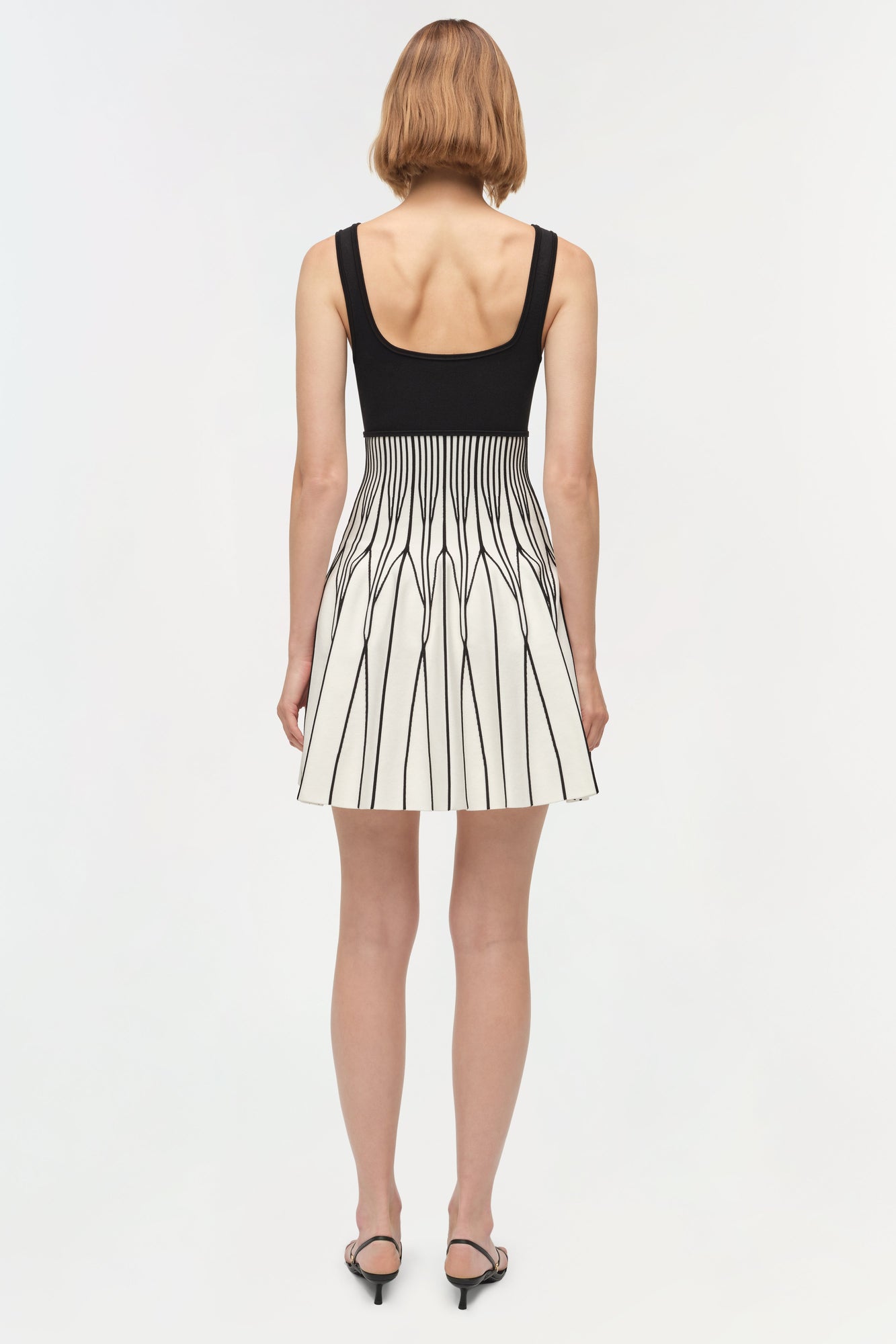 Black and white knit mini dress with sleeveless design and pleated skirt worn with black heels.