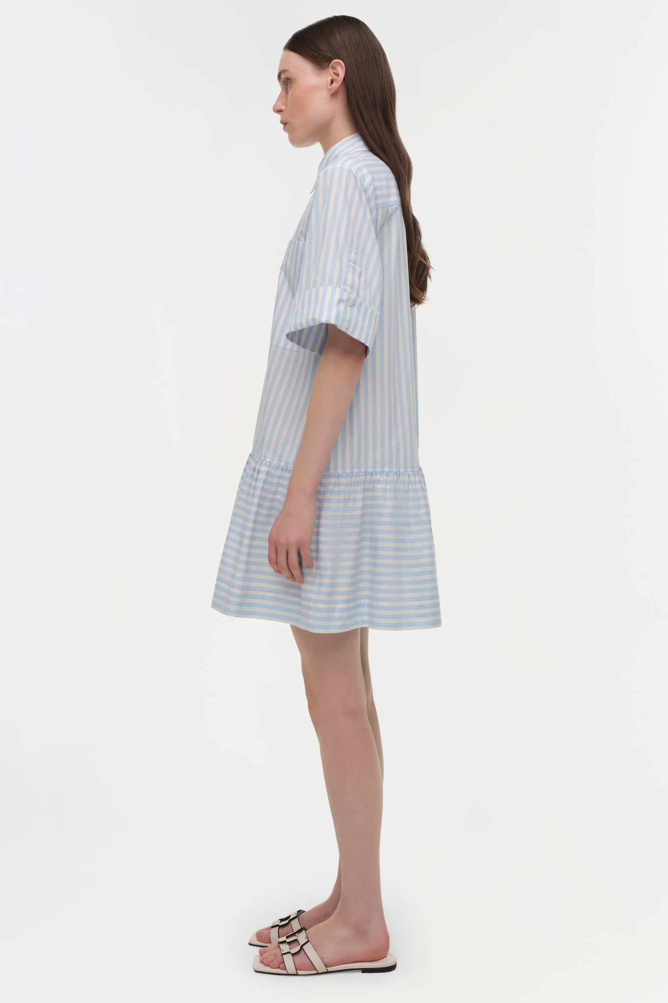 Blue and white striped cotton shirt dress with short sleeves and gathered hem, shown on model in profile view.
