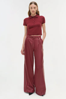 Burgundy leather wide-leg pants with high waist and pleated front, shown with matching short-sleeve polo top.