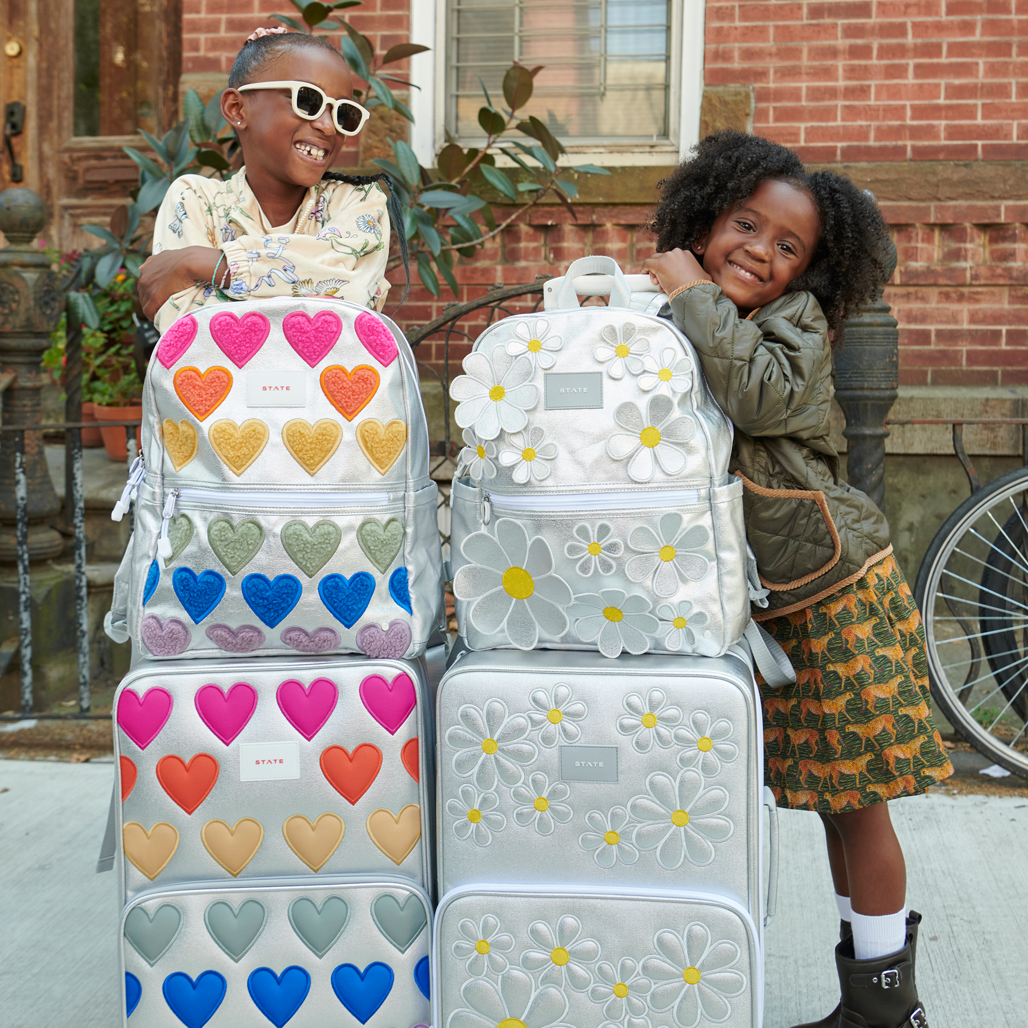 Two girls with STATE Bags Travel Bundles in Patchwork Hearts and 3D Daisies