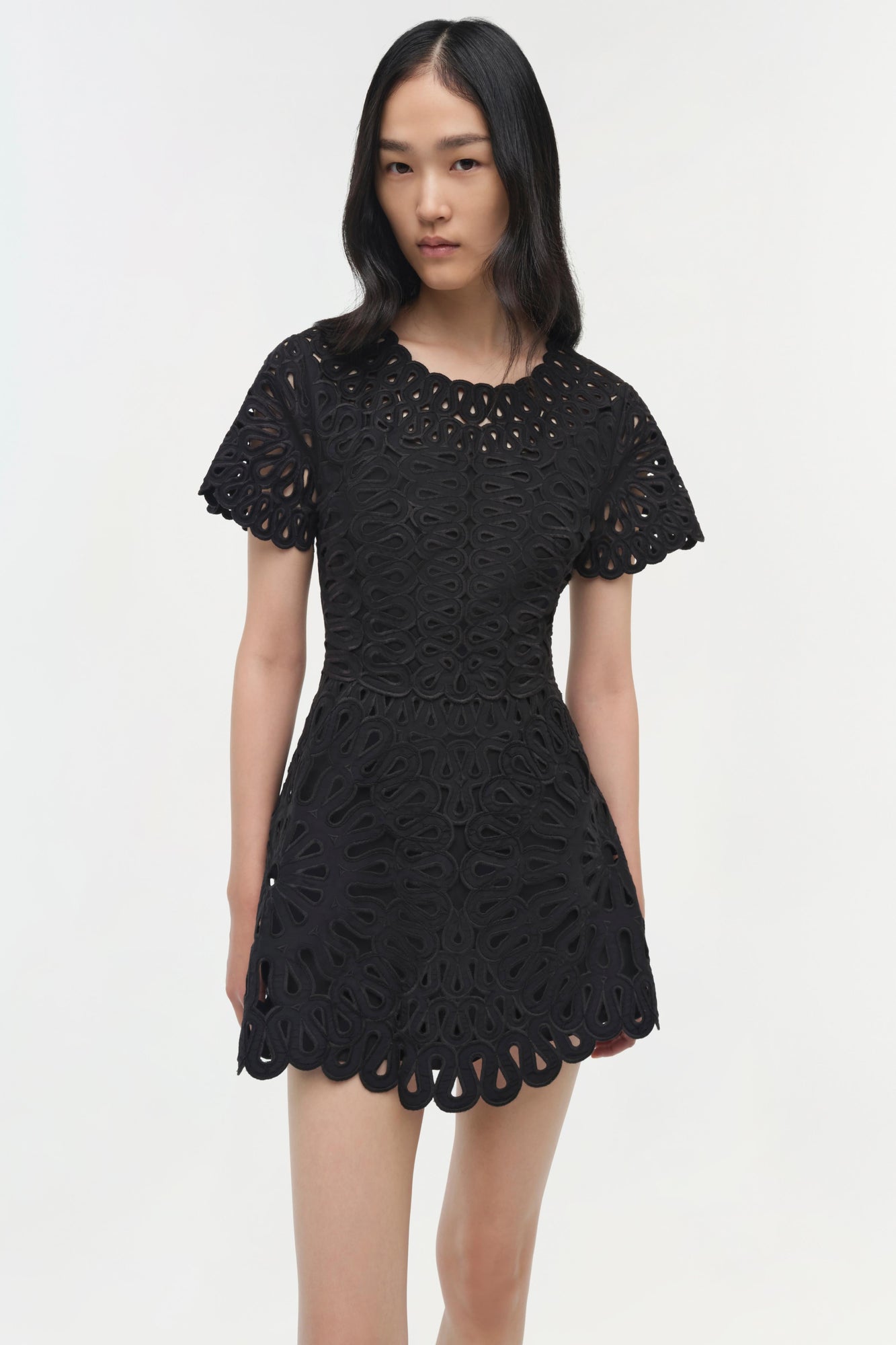 Black mini dress with allover eyelet embroidery, short puffed sleeves, and scalloped hem.