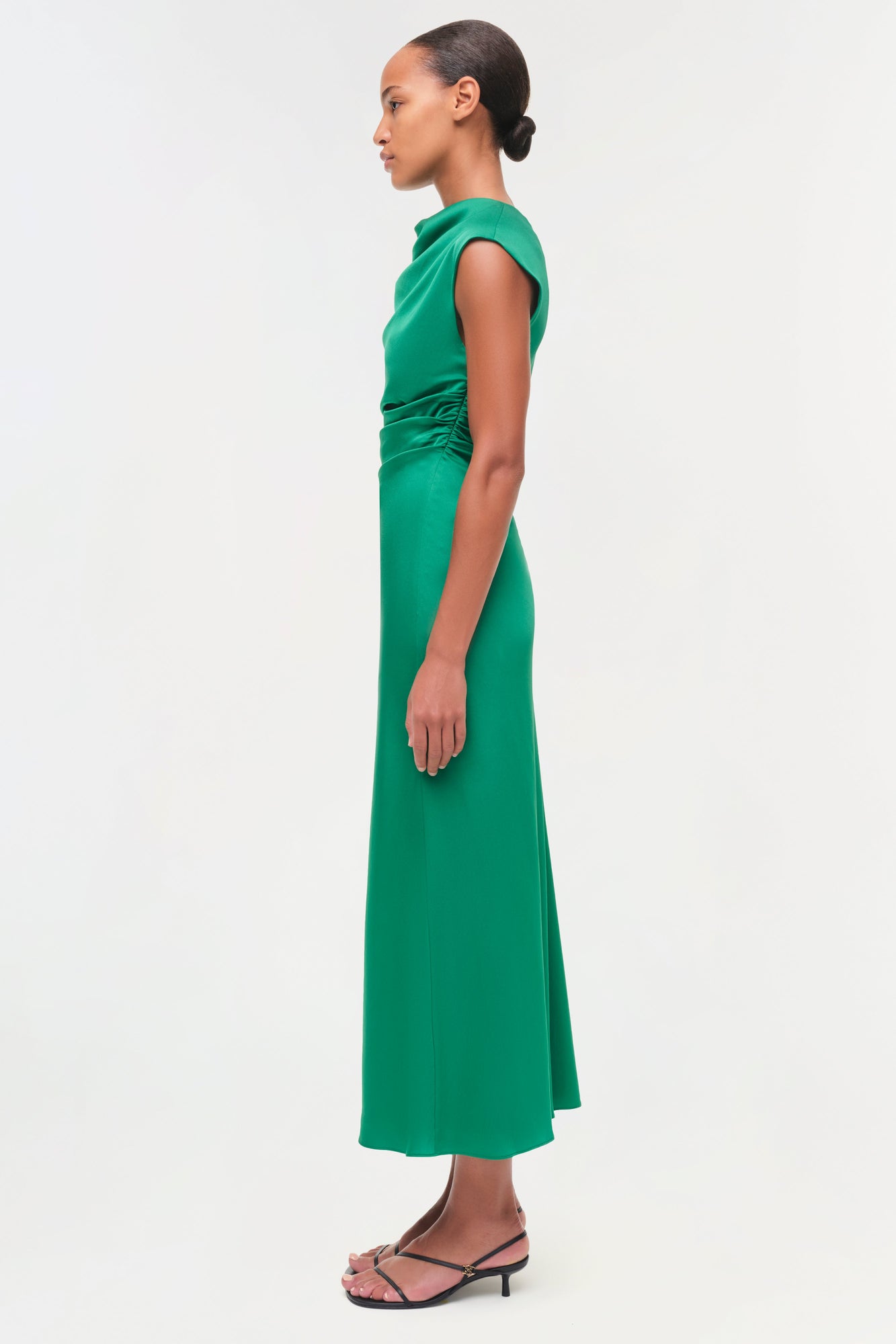 Green satin midi dress with draped shoulder detail and ruched side, shown on model in profile view.