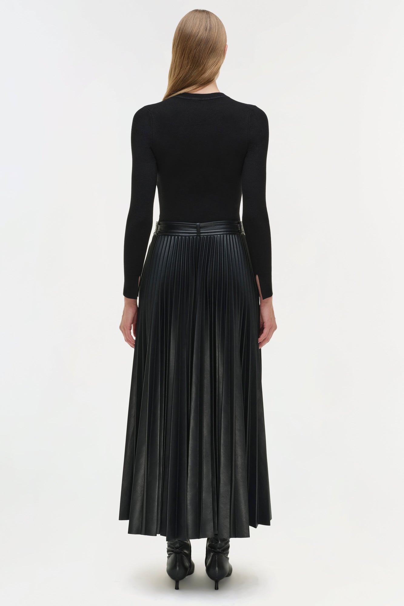 Woman wearing black knit midi dress with long sleeves and pleated faux-leather skirt, shown from back.