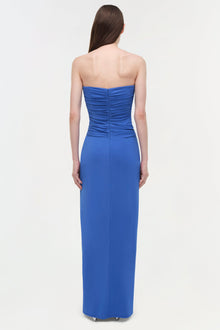 Woman wearing a blue strapless floor-length gown with ruched draped bustier detail, shown from back view.