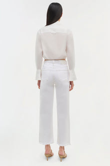 Woman wearing cream cropped long-sleeve top with flared cuffs and white cropped jeans, shown from back.