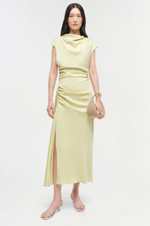 Pale yellow satin midi dress with cowl neckline, ruched waist, and side slit, worn with white strappy sandals.