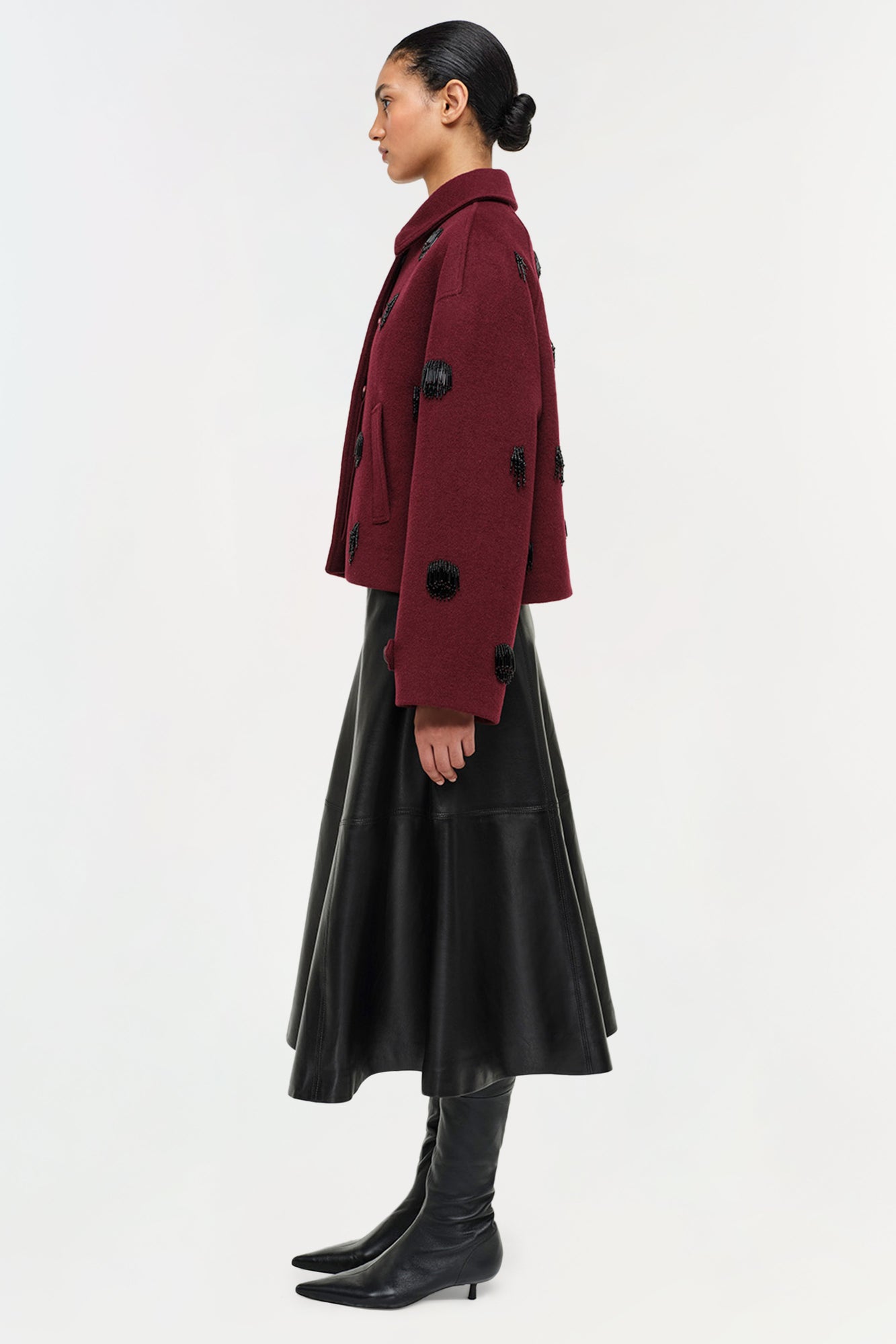 Black leather midi skirt with A-line silhouette, styled with burgundy cardigan and black boots.