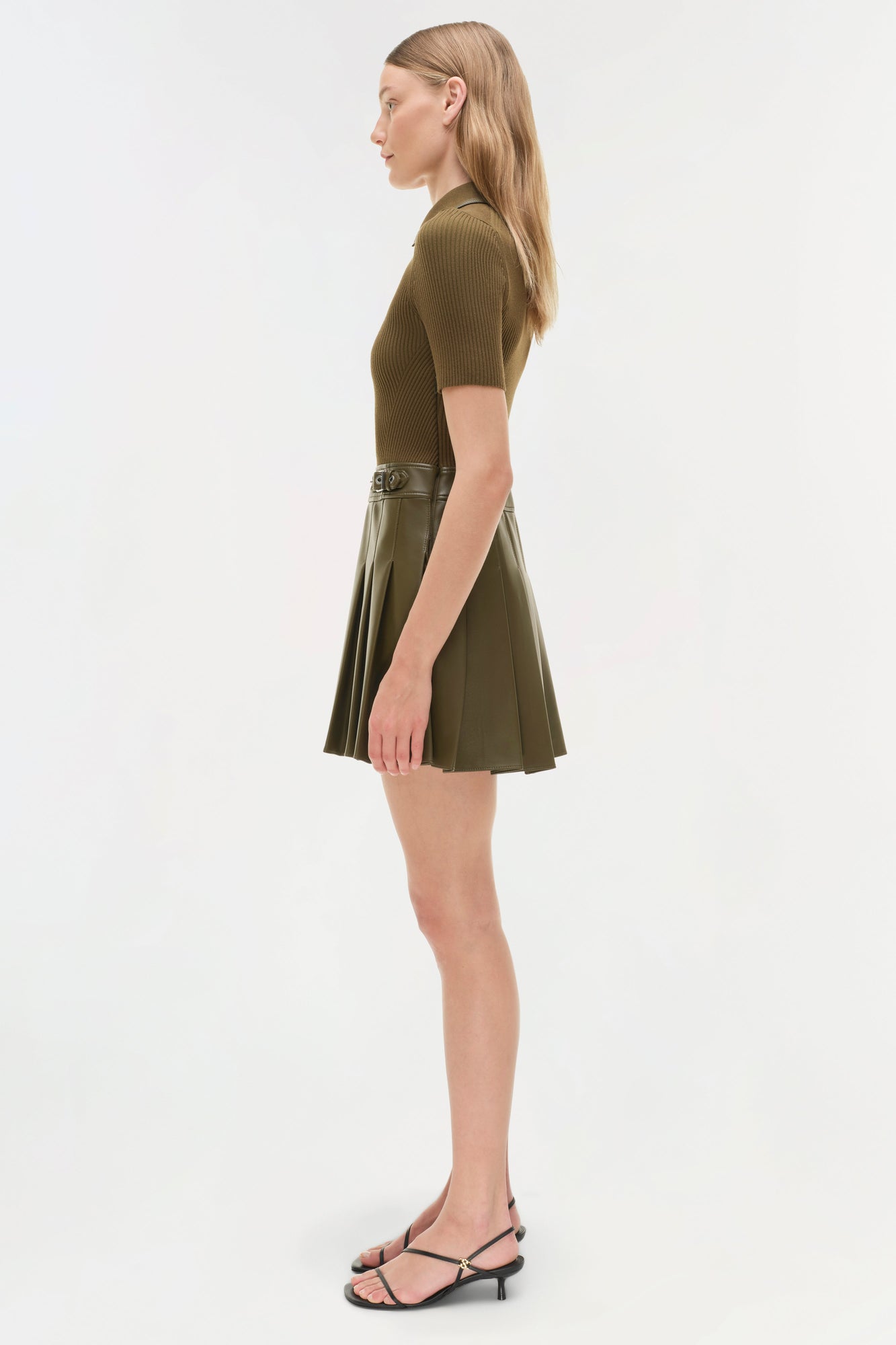 Olive green mini dress with ribbed knit top and pleated skirt, belted waist, shown on model in side profile.