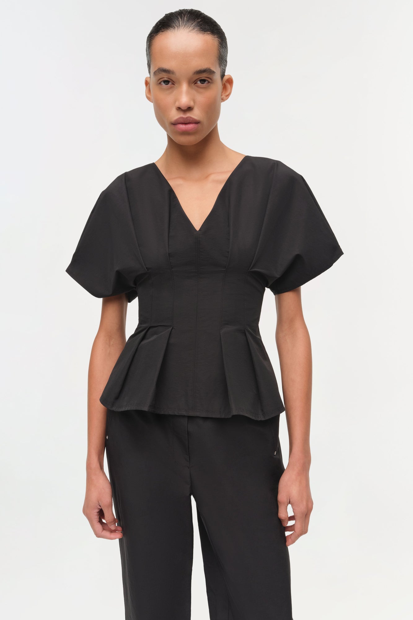 Woman wearing black cotton faille pull-on pants with a matching peplum top.