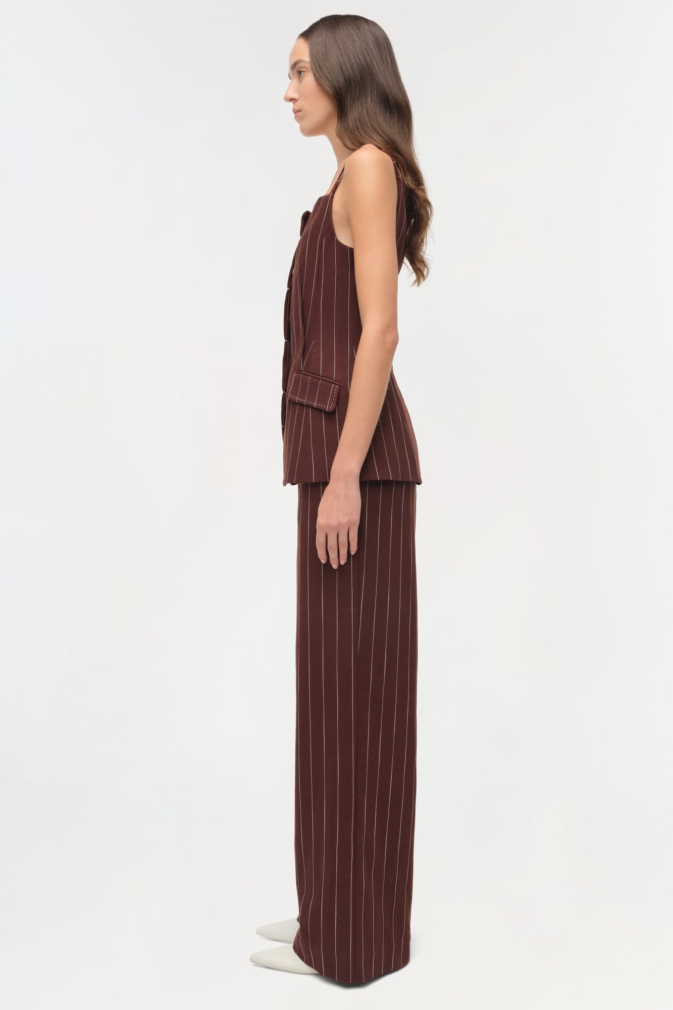Woman wearing burgundy pinstriped suiting pants with matching sleeveless vest, shown in side profile.