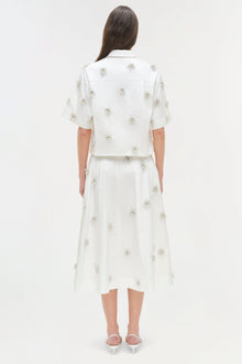 White camp shirt with silver beaded flower embellishments throughout, shown on model from back view.
