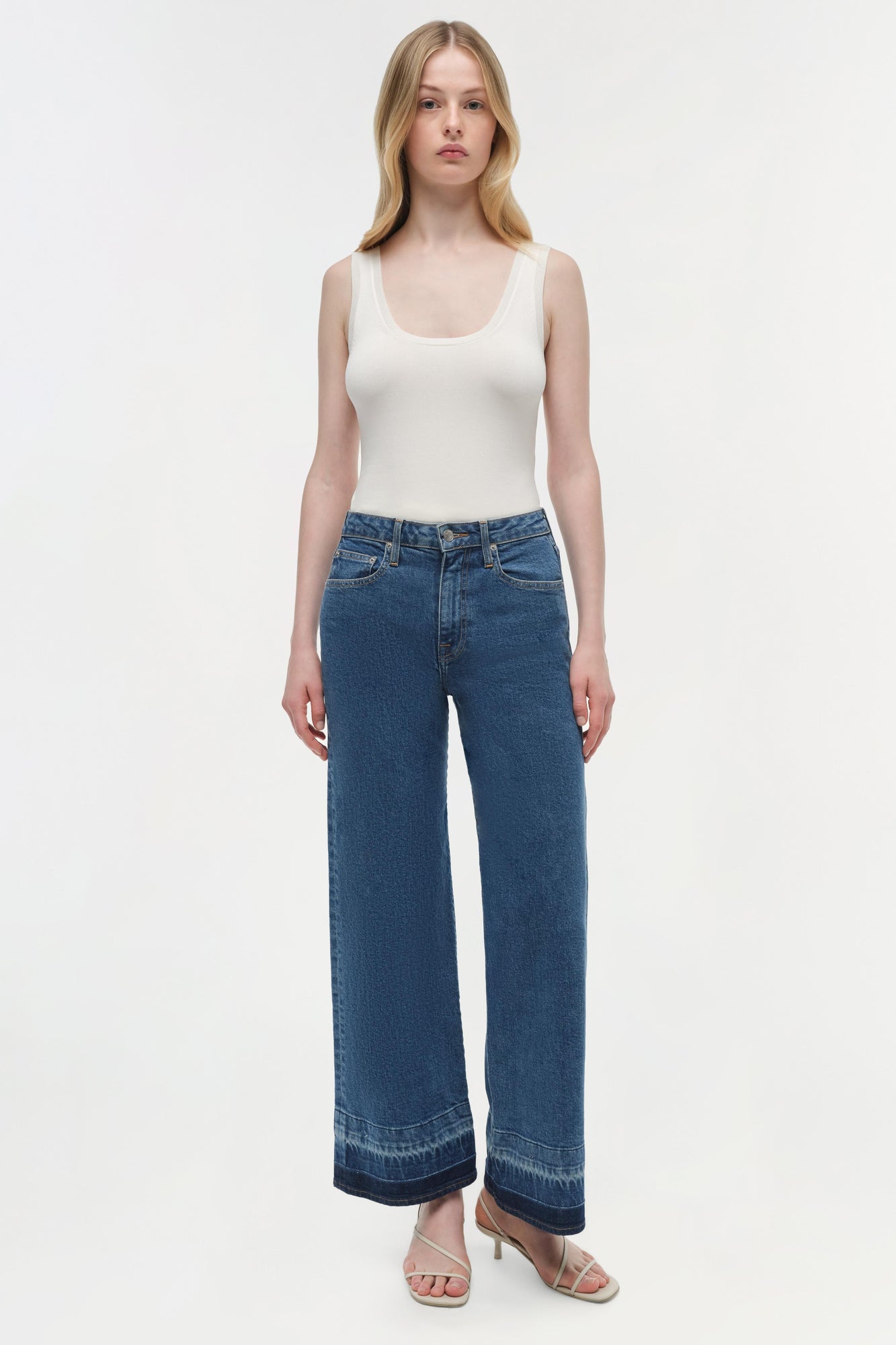 Woman wearing white sleeveless tank top and medium wash wide-leg cropped jeans with darker hem detail.