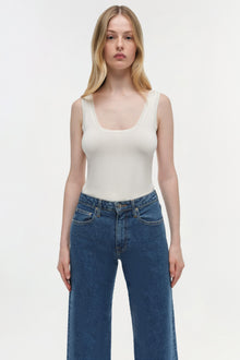 Woman wearing cream sleeveless tank top and blue wide-leg cropped denim jeans.