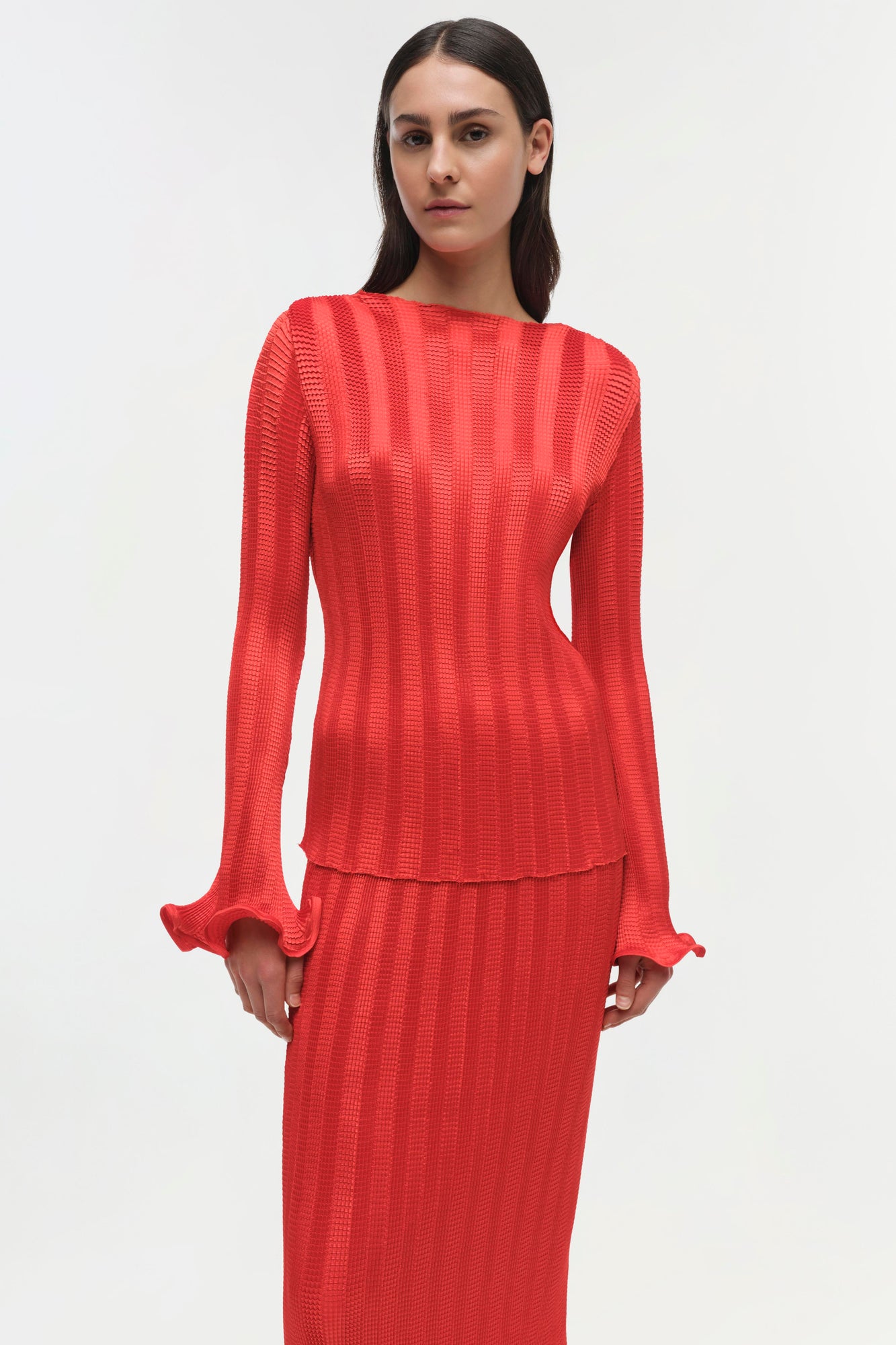 Woman wearing a red ribbed long-sleeve top with ruched cuffs and a fitted silhouette.