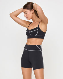 Side view of the LSPACE Eclipse Bra in black on a model against a white background, paired with matching black-cream active shorts, showing the profile of the sports bra.