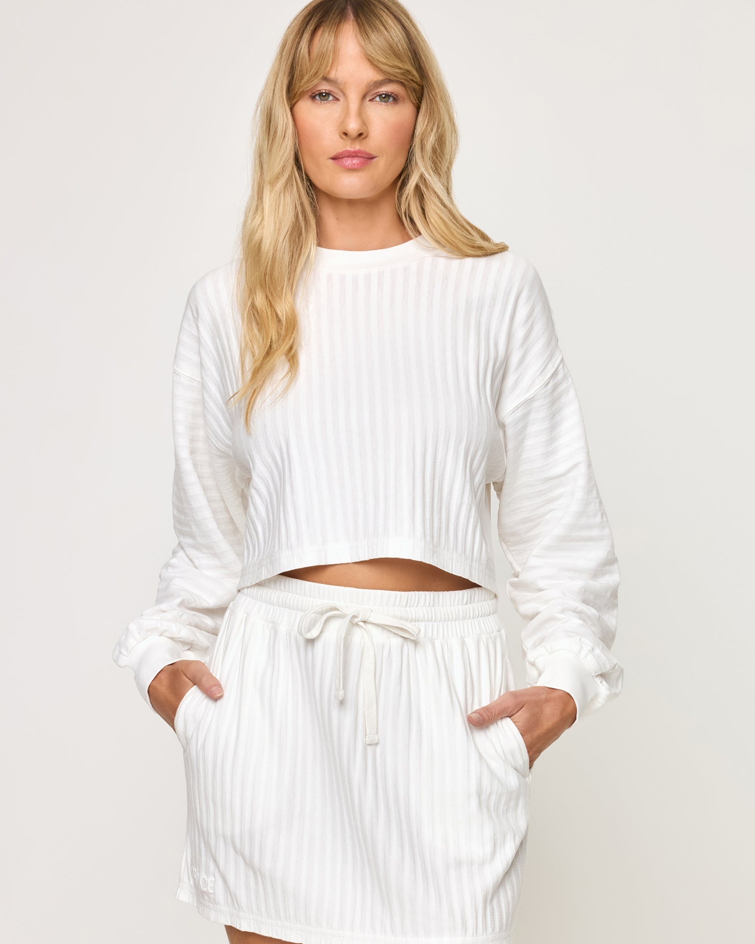 Close-up front view of model wearing the Half Court Skirt in white with matching white Half Court Pullover, hands in pockets.