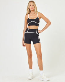 Front view of model wearing the Revel Short in black-cream with matching black-cream Revel Top and white sneakers.