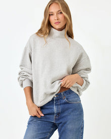 Front studio three-quarter torso view of the Crush Sweatshirt in Heather Gray, a heather gray oversized quarter-zip pullover sweatshirt with a mock neck, styled with blue denim jeans.
