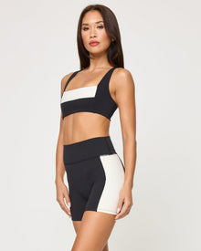 Side view of the LSPACE Uppercut Bra in black-cream on a model against a white background, paired with matching black-cream high-rise active shorts, showing the profile silhouette.