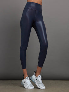 Model is wearing navy high waisted performance leggings in a liquidy-shine finish that hit at mid to low calf.