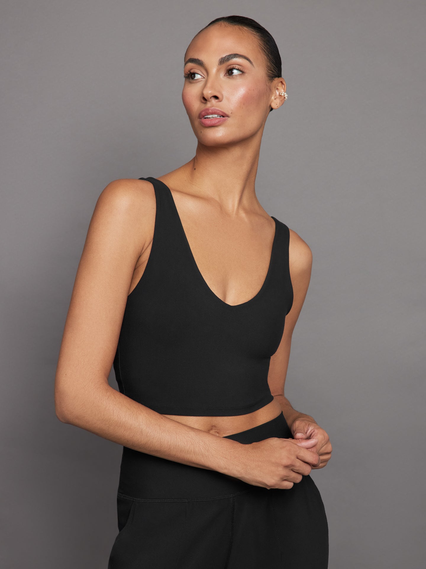 Model wears a black, longline sports bra with a deep V-neck front and an open V-shaped back, made from sleek, smooth fabric.
