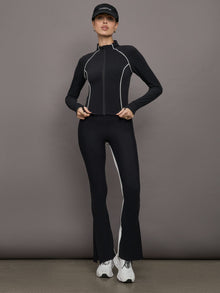 Model wears a black mock neck long sleeve top with thumb holes with thin white stripes outlining a corseted physique.