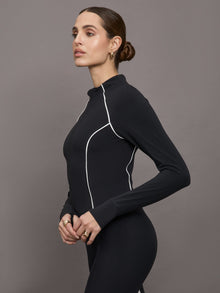 Model wears a black mock neck long sleeve top with thumb holes with thin white stripes outlining a corseted physique.