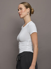 Model wears a short sleeved, ribbed jersey fitted white top with ruching down both sides. 