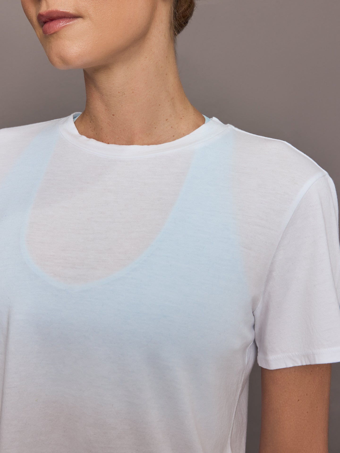 Model wears a cropped boxy white sheer tee shirt. 