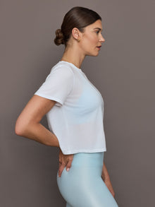 Model wears a cropped boxy white sheer tee shirt. 