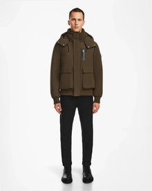 A person stands facing forward in an urban style, wearing the Rudsak ASH - 6124599 Army mens down bomber jacket with large front pockets, black pants, and black shoes against a plain white background.