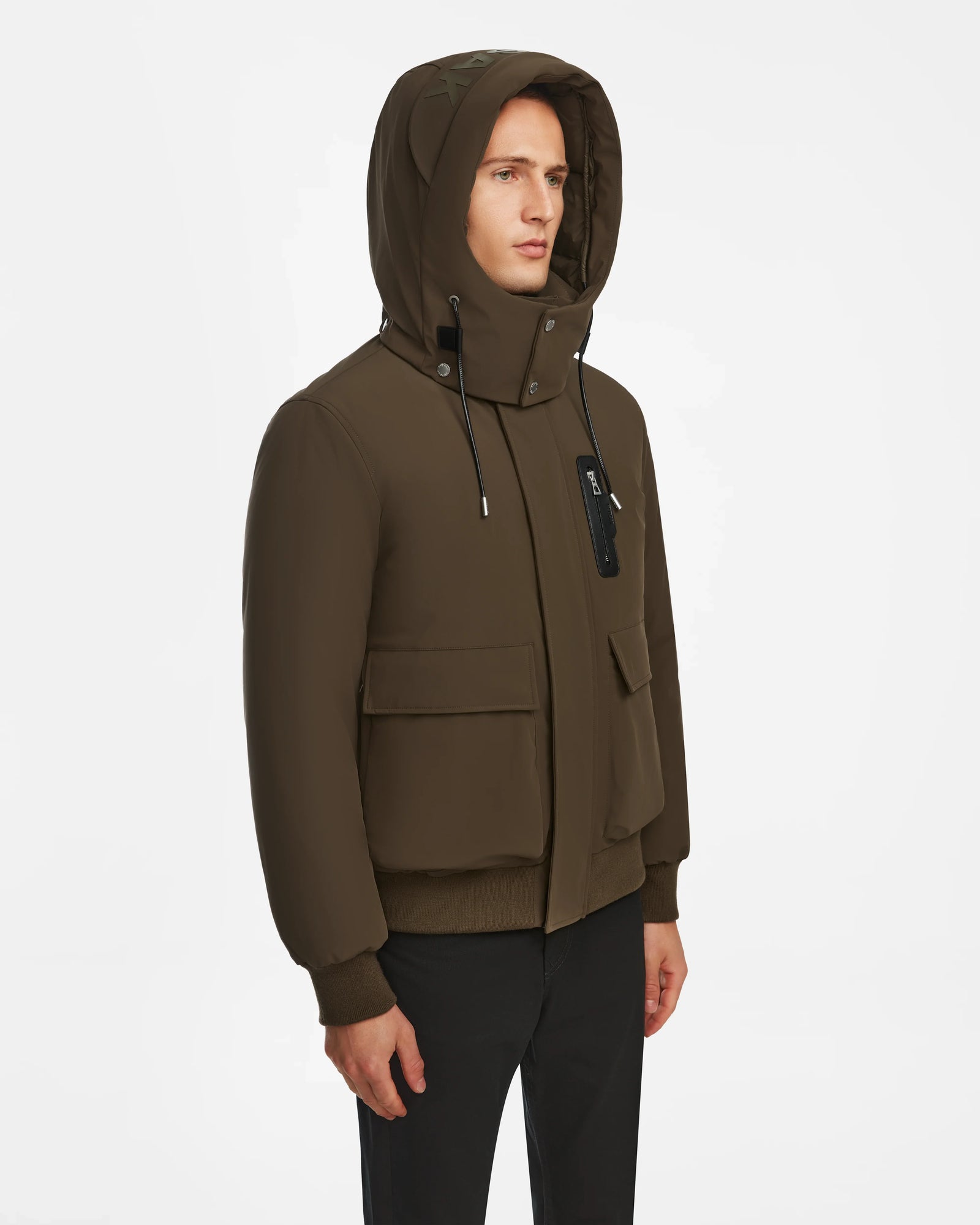 Model wears the Rudsak ASH - 6124599 Army mens down bomber jacket in dark olive, with front pockets, ribbed cuffs, and black drawstrings, styled with black pants against a white background for an urban look.