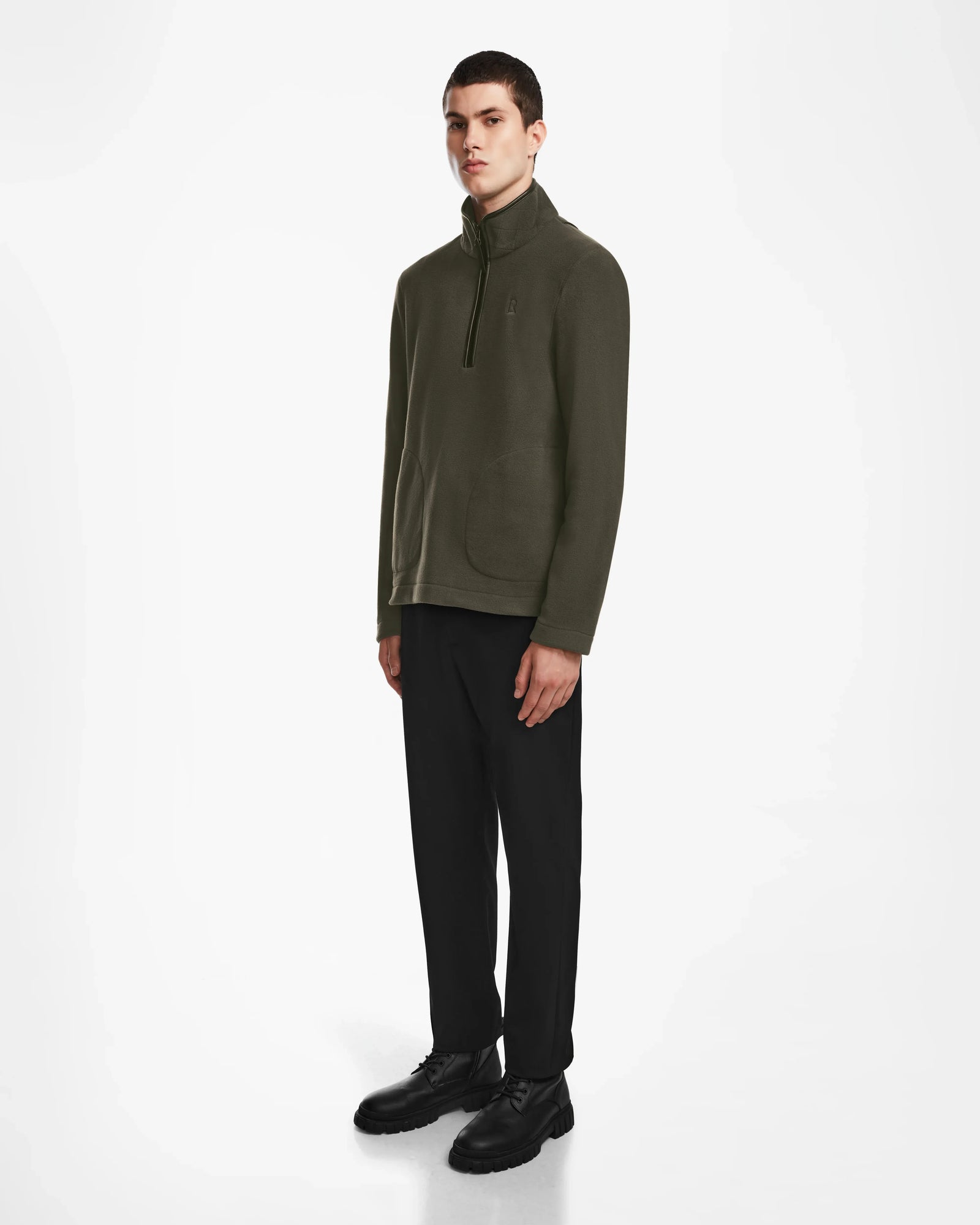 A young man stands against a white background wearing the Rudsak BECK - 6524538 Army men’s fleece pullover with vegan leather trims, paired with black pants and shoes. He faces forward, hands by his sides, with a neutral expression.