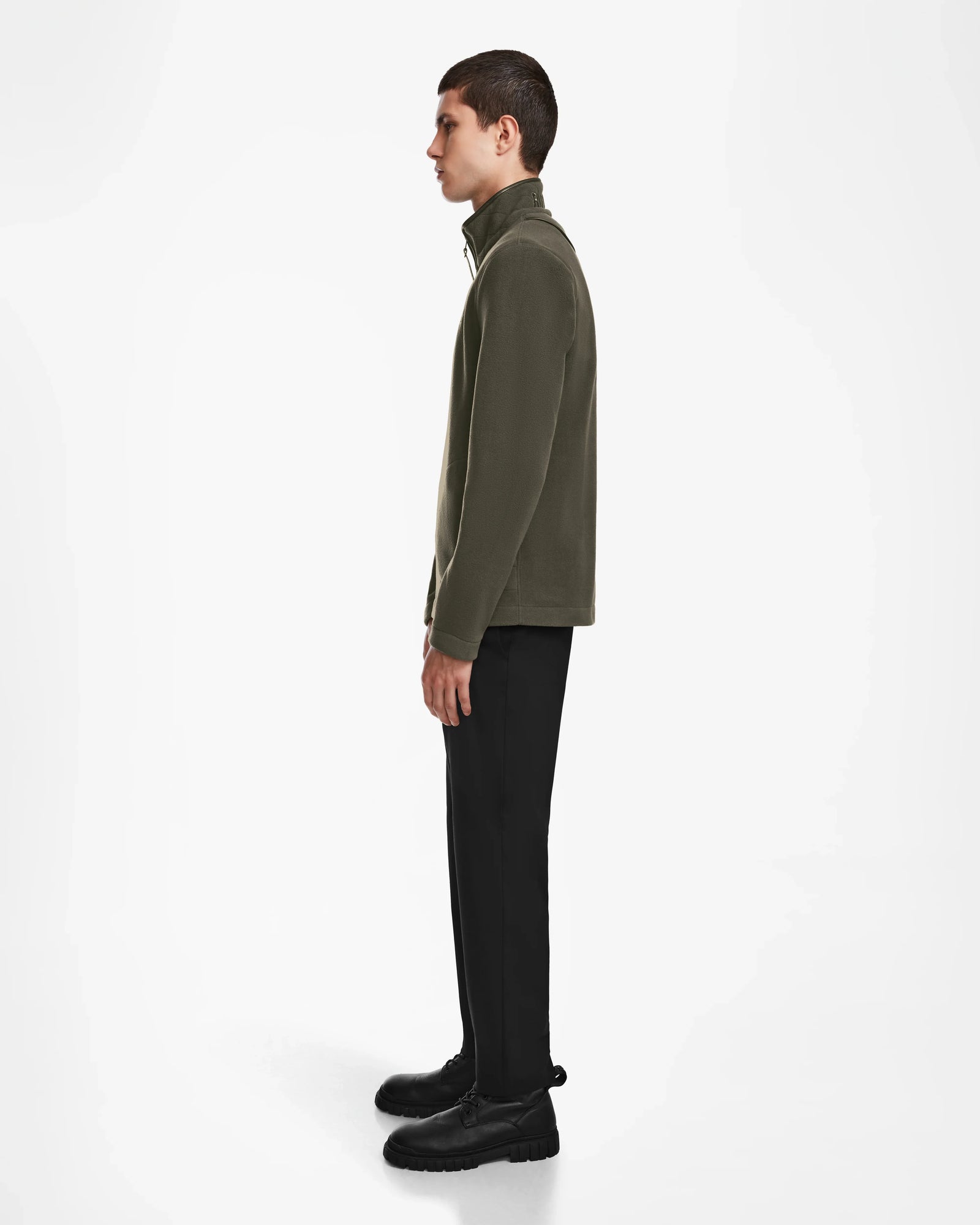 A person stands in profile against a white background, wearing the Rudsak BECK - 6524538 Army half-zip pullover featuring vegan leather trims, paired with black pants and shoes.