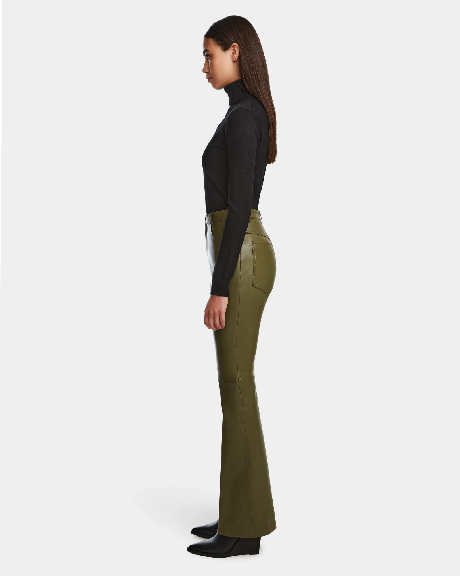 Woman in profile against a white background, wearing a fitted black turtleneck, CARISSA - 8524545 Loden Green leather pants by Rudsak with a high-waisted flared silhouette, and black ankle boots.