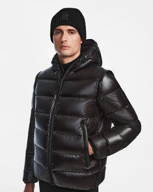 A person wears the Rudsak DEMIAN S-R - M123505 Black mens down puffer jacket with a hood and a black knit beanie, standing against a plain white background. This RDS-certified jacket delivers premium warmth and sleek style.