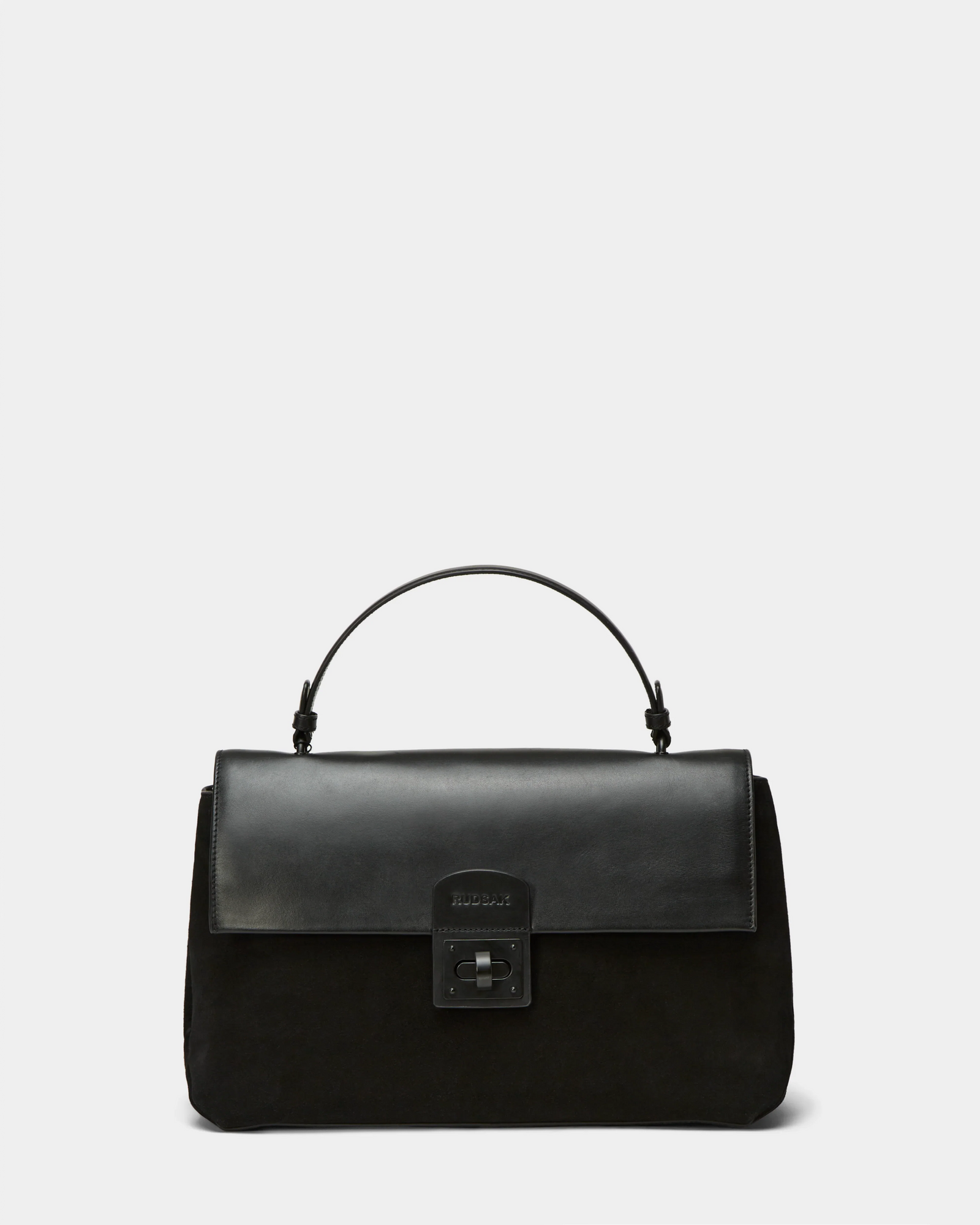 The Rudsak ESMA - 8324519 Black is a black suede and leather handbag with a top handle, front flap with rectangular metal clasp, and removable shoulder strap, shown against a plain light gray background.